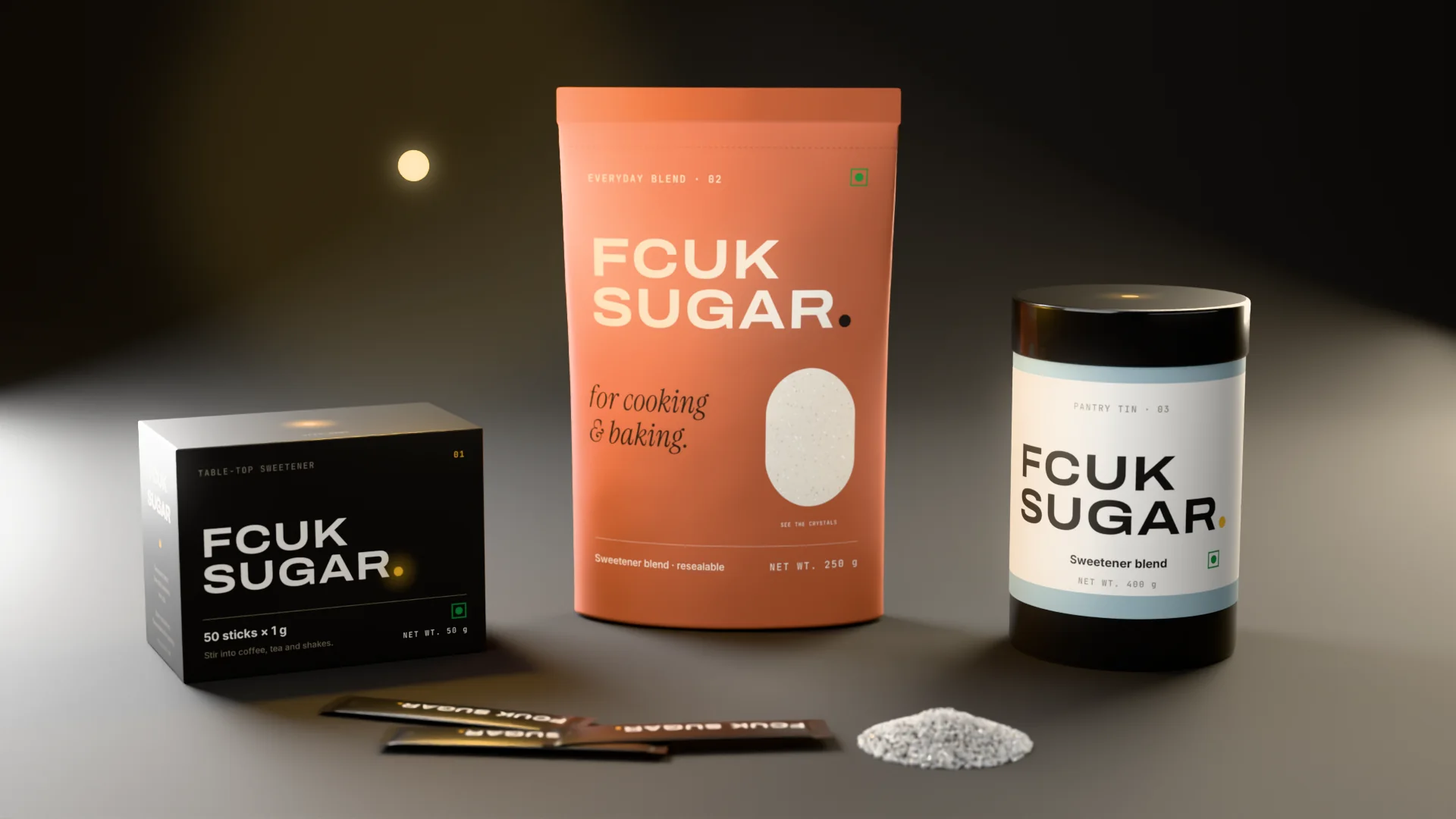 The FCUK SUGAR range — stick carton, Everyday Blend pouch, Pantry Tin and loose crystals — under a single point of warm light.